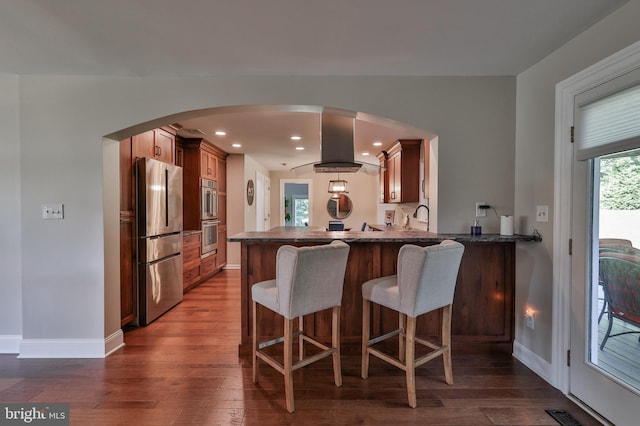 kitchen with stainless steel appliances, dark hardwood / wood-style floors, kitchen peninsula, island range hood, and a breakfast bar