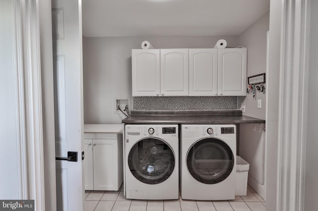 washroom with light tile patterned flooring, cabinets, and washing machine and clothes dryer