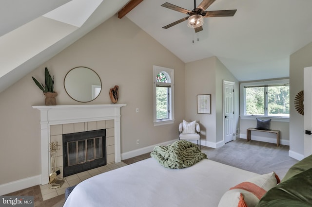 bedroom featuring ceiling fan, multiple windows, lofted ceiling with beams, and a tiled fireplace