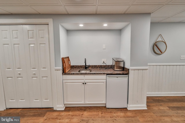 bar with light hardwood / wood-style flooring, dark stone countertops, dishwasher, white cabinets, and sink