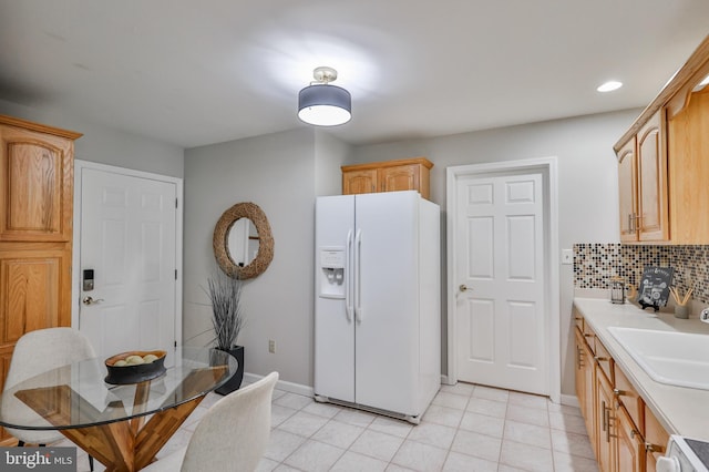 kitchen with backsplash, stove, sink, light brown cabinets, and white fridge with ice dispenser