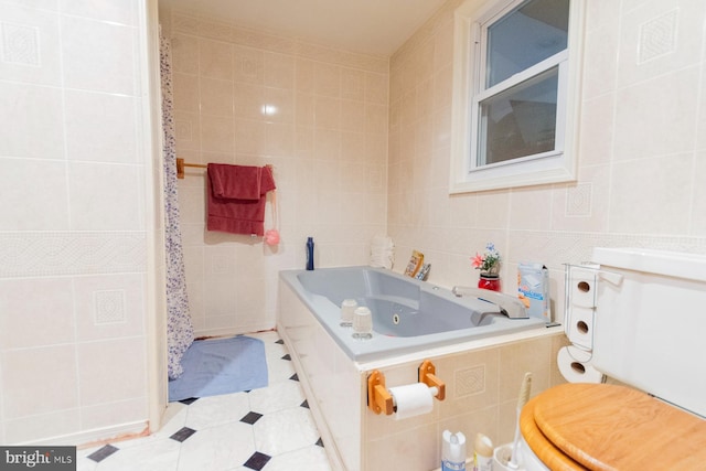 bathroom with a relaxing tiled tub, toilet, tile patterned flooring, and tile walls