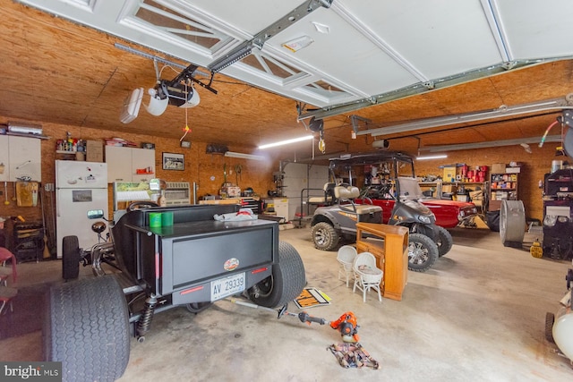 garage featuring white refrigerator, a garage door opener, and a workshop area