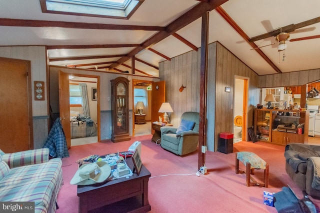 carpeted living room with ceiling fan, wooden walls, and vaulted ceiling with skylight