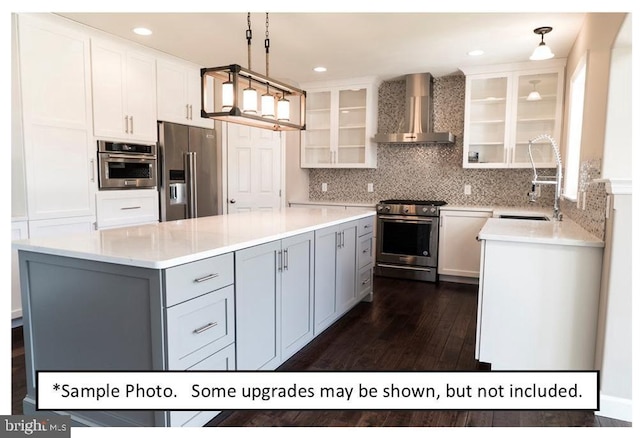 kitchen with white cabinets, wall chimney range hood, high end appliances, sink, and hanging light fixtures