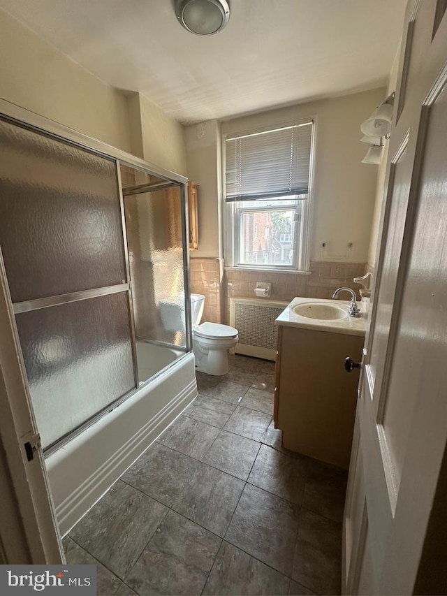 full bathroom featuring radiator heating unit, toilet, vanity, tile patterned floors, and tile walls