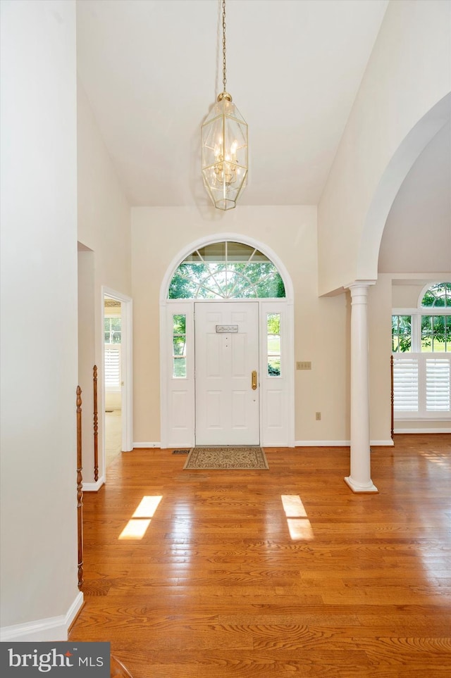 foyer entrance featuring decorative columns, hardwood / wood-style floors, and a chandelier