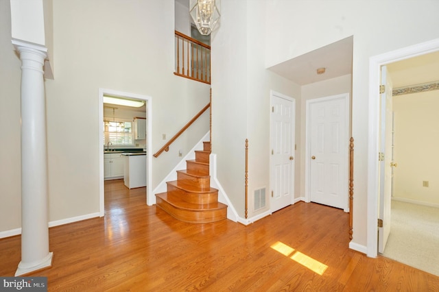 foyer entrance featuring a towering ceiling, ornate columns, and light wood-type flooring