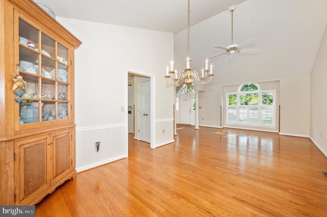 unfurnished dining area with light wood-type flooring, high vaulted ceiling, and ceiling fan with notable chandelier