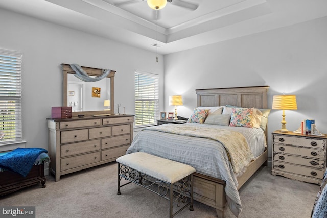 bedroom with light carpet, ceiling fan, and a tray ceiling