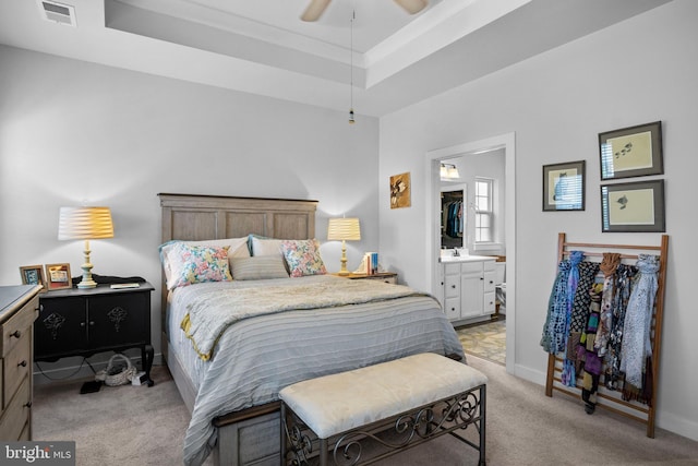 bedroom with ceiling fan, ensuite bathroom, a raised ceiling, and light carpet