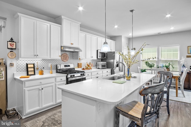 kitchen featuring a kitchen bar, a center island with sink, appliances with stainless steel finishes, decorative light fixtures, and sink