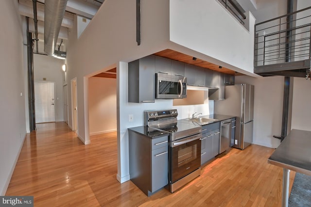 kitchen with light wood-type flooring, stainless steel appliances, a towering ceiling, and sink