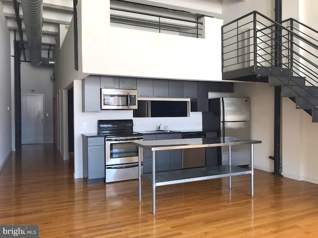 kitchen featuring a kitchen bar, stainless steel appliances, light wood-type flooring, a towering ceiling, and sink