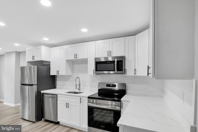 kitchen with white cabinets, appliances with stainless steel finishes, sink, light stone counters, and light hardwood / wood-style flooring