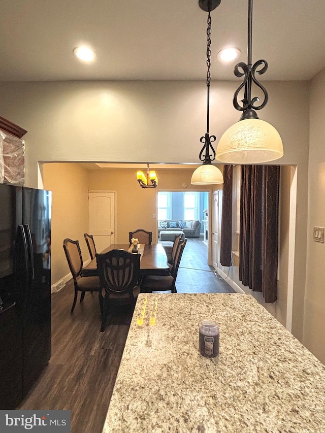 kitchen with a notable chandelier, wood-type flooring, black refrigerator, hanging light fixtures, and light stone countertops