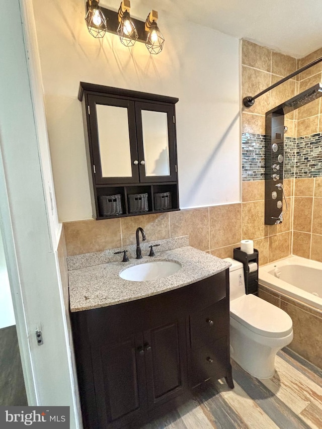 full bathroom with tiled shower / bath, backsplash, toilet, vanity, and tile walls