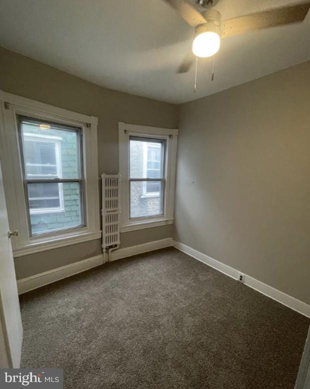 carpeted empty room with ceiling fan and radiator