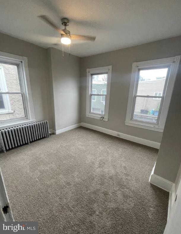 carpeted empty room with ceiling fan and radiator