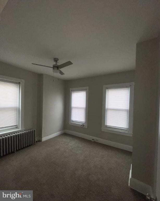 empty room with ceiling fan, radiator, and dark carpet