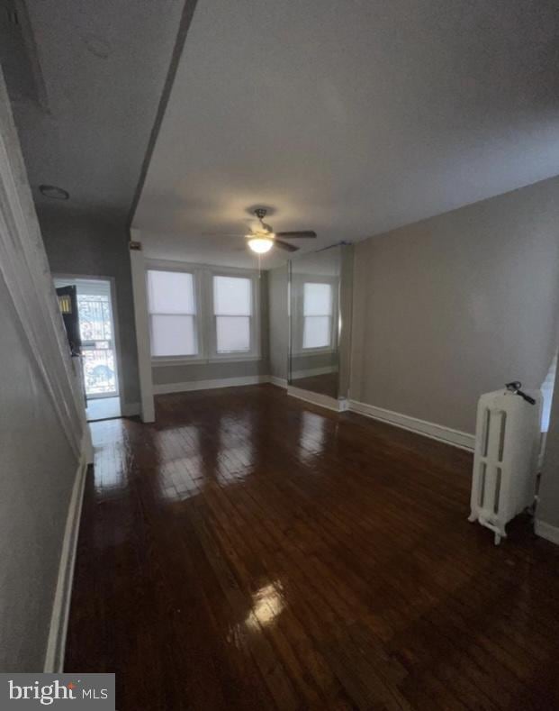 unfurnished living room featuring ceiling fan, radiator, and dark wood-type flooring