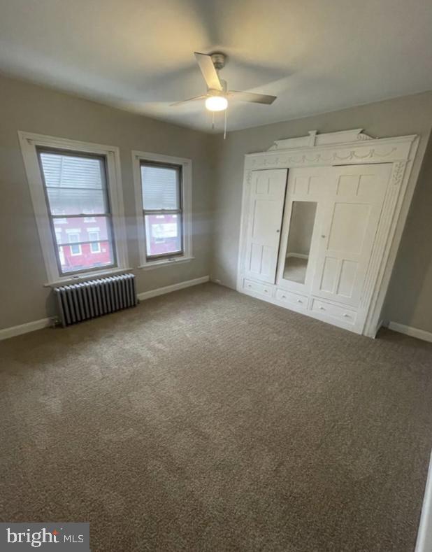 unfurnished bedroom with ceiling fan, carpet floors, and radiator heating unit