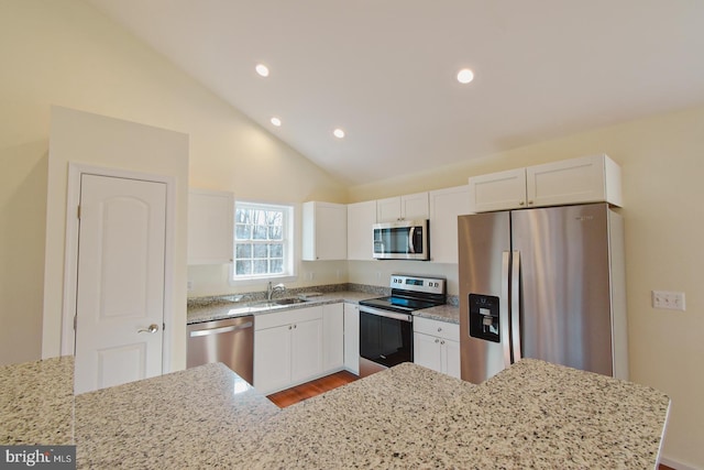 kitchen with light stone counters, white cabinetry, stainless steel appliances, and lofted ceiling