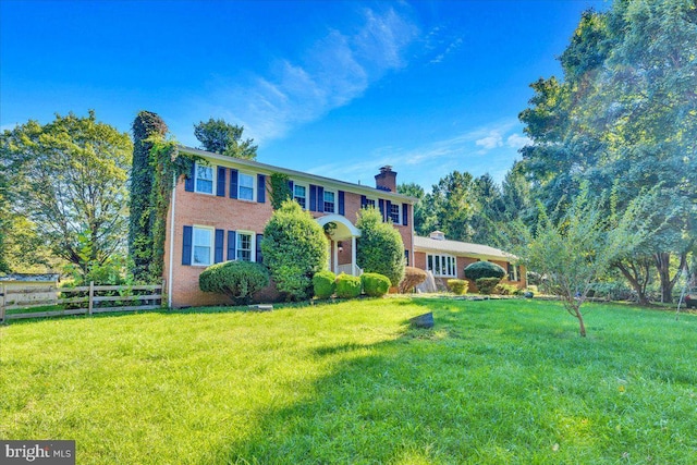 colonial home featuring brick siding, a front yard, a chimney, and fence