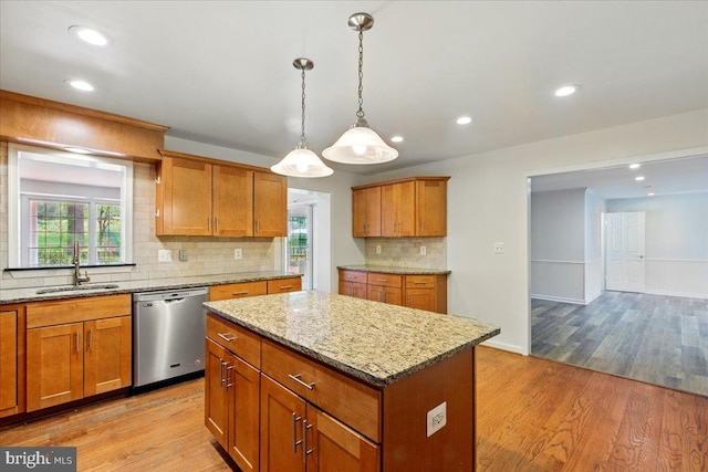 kitchen featuring light stone counters, stainless steel dishwasher, a sink, light wood-style floors, and decorative backsplash