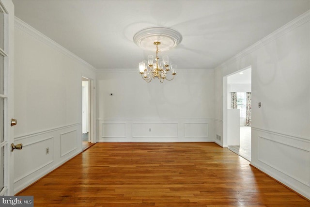 unfurnished dining area with a decorative wall, wood finished floors, a notable chandelier, and crown molding