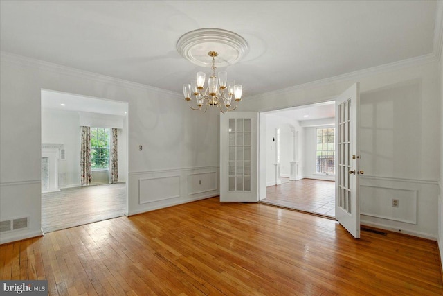 unfurnished dining area featuring visible vents, french doors, wood-type flooring, a decorative wall, and a chandelier