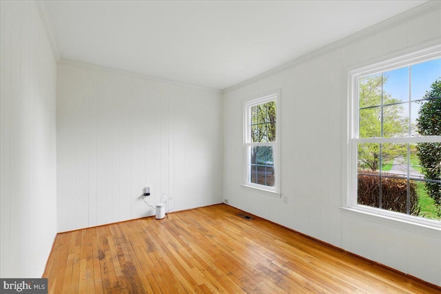 spare room featuring plenty of natural light, ornamental molding, visible vents, and light wood-type flooring