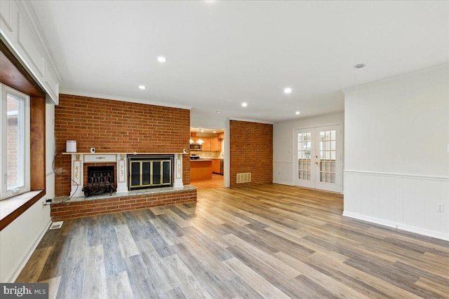 unfurnished living room with a brick fireplace, visible vents, light wood finished floors, and ornamental molding