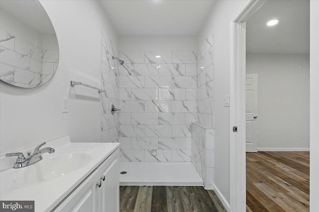 bathroom featuring a tile shower, baseboards, vanity, and wood finished floors