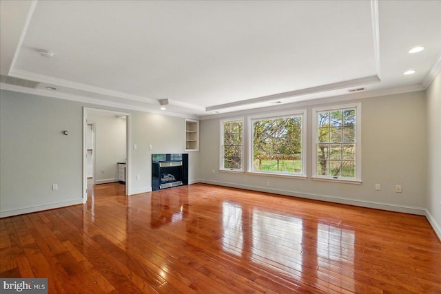 unfurnished living room featuring hardwood / wood-style flooring, a high end fireplace, a tray ceiling, ornamental molding, and visible vents