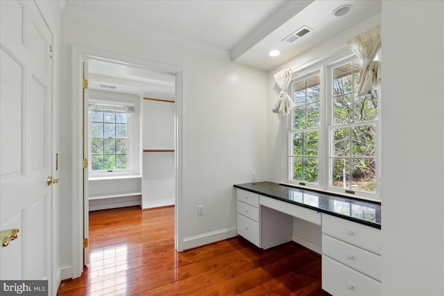 unfurnished office with crown molding, built in study area, visible vents, baseboards, and dark wood-style floors