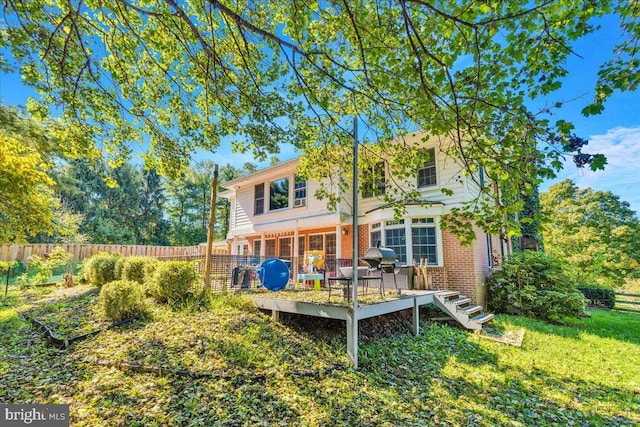 rear view of property featuring fence, a lawn, brick siding, and a deck