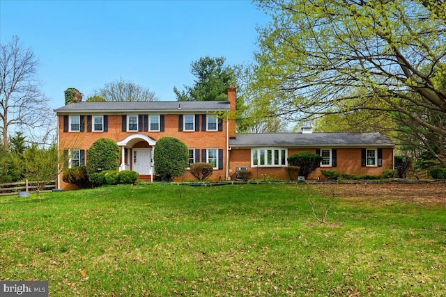 colonial home featuring brick siding, a front yard, and a chimney