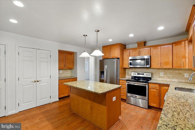 kitchen featuring a sink, light wood-type flooring, stainless steel appliances, backsplash, and a kitchen island