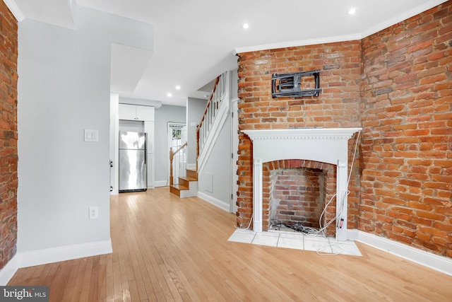 unfurnished living room with brick wall, crown molding, and light hardwood / wood-style floors