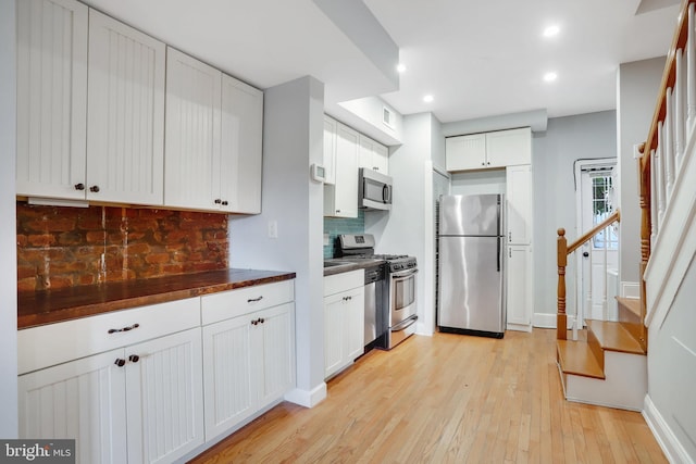 kitchen featuring white cabinetry, butcher block counters, appliances with stainless steel finishes, backsplash, and light wood-type flooring