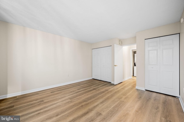 unfurnished bedroom featuring multiple closets and light hardwood / wood-style floors