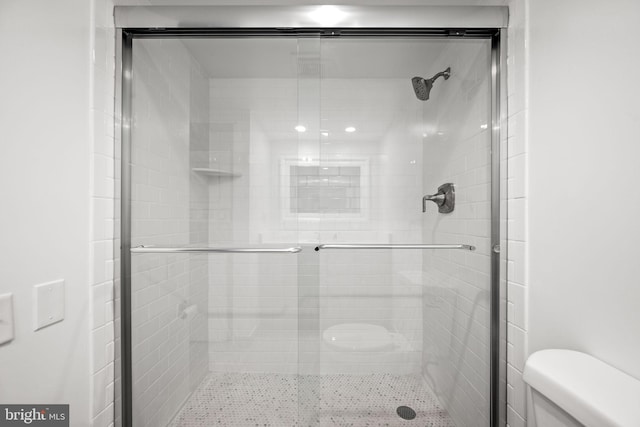 bathroom featuring a shower with door and toilet