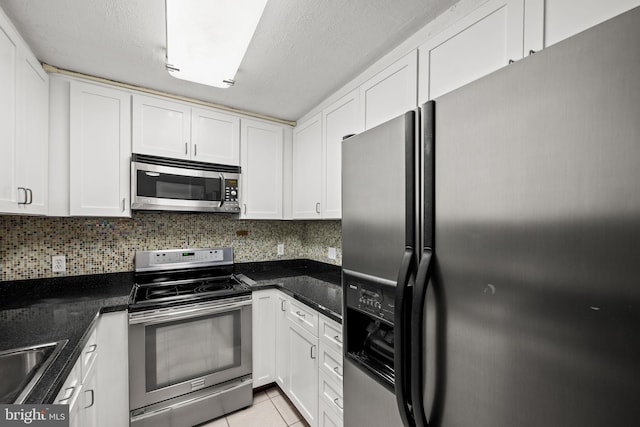 kitchen with white cabinetry, backsplash, dark stone countertops, stainless steel appliances, and light tile patterned flooring