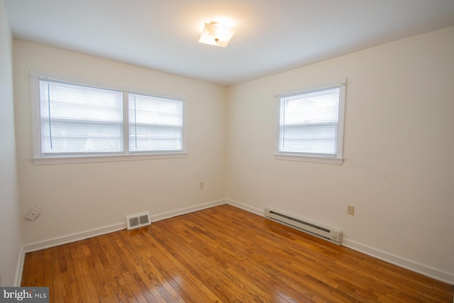 empty room featuring a baseboard heating unit and hardwood / wood-style flooring