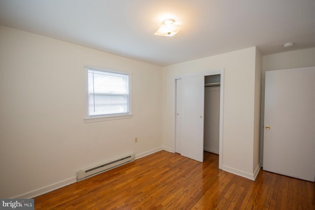 unfurnished bedroom featuring baseboard heating, hardwood / wood-style floors, and a closet