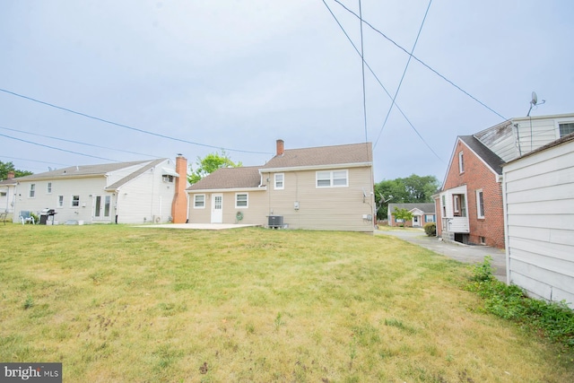 rear view of property with central air condition unit and a lawn