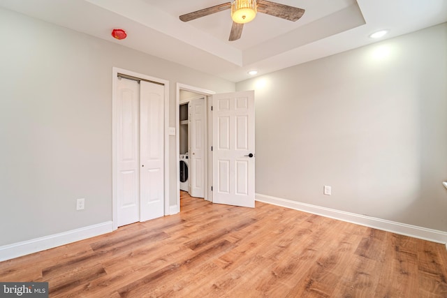 unfurnished bedroom with light wood-type flooring, ceiling fan, a closet, and a raised ceiling