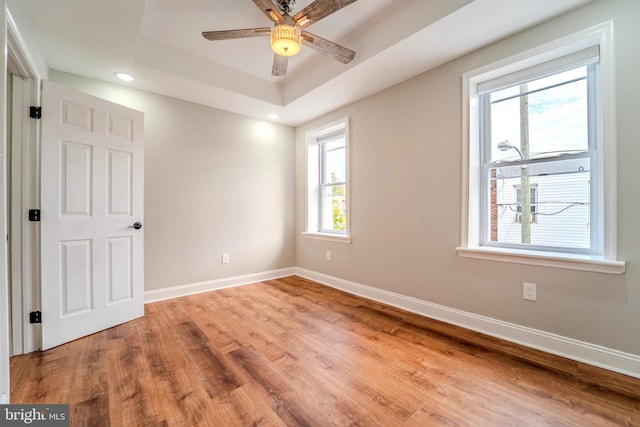 spare room with ceiling fan, plenty of natural light, a tray ceiling, and light hardwood / wood-style flooring