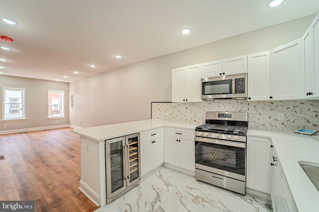 kitchen with kitchen peninsula, appliances with stainless steel finishes, decorative backsplash, beverage cooler, and white cabinets